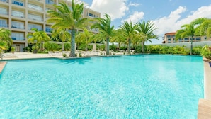 A clear blue pool surrounded by palm trees and a multi-story hotel building. - Aruba Eagle Beach One Happy Island Vacation Waiting For You!! (Oranjestad-West)