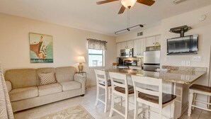 A living room with a sofa, a coffee table, and a TV. There is a kitchen with a stove, microwave, and refrigerator. - Welcome to beautiful Gulf Shores! *Location!! Location!! Location!!* #TheHangout (Gulf Shores)