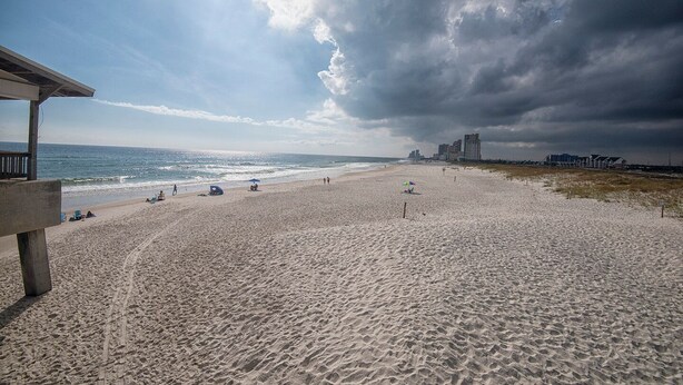 A beach with a wooden structure, a sandy shore, and a city skyline in the background. - Welcome to beautiful Gulf Shores! *Location!! Location!! Location!!* #TheHangout (Gulf Shores)