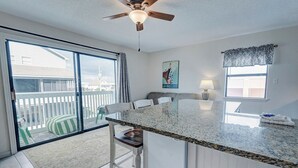 A modern kitchen with a granite countertop, a ceiling fan, and a sliding glass door leading to a balcony. - Welcome to beautiful Gulf Shores! *Location!! Location!! Location!!* #TheHangout (Gulf Shores)
