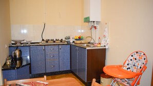 Una cocina compacta con armarios azules, una estufa a gas y un lavamanos. Hay una pequeña mesa de comedor con mantel estampado y una trona.