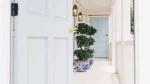 Een witte veranda met een lichtblauwe deur, een bloempot en een lamp.