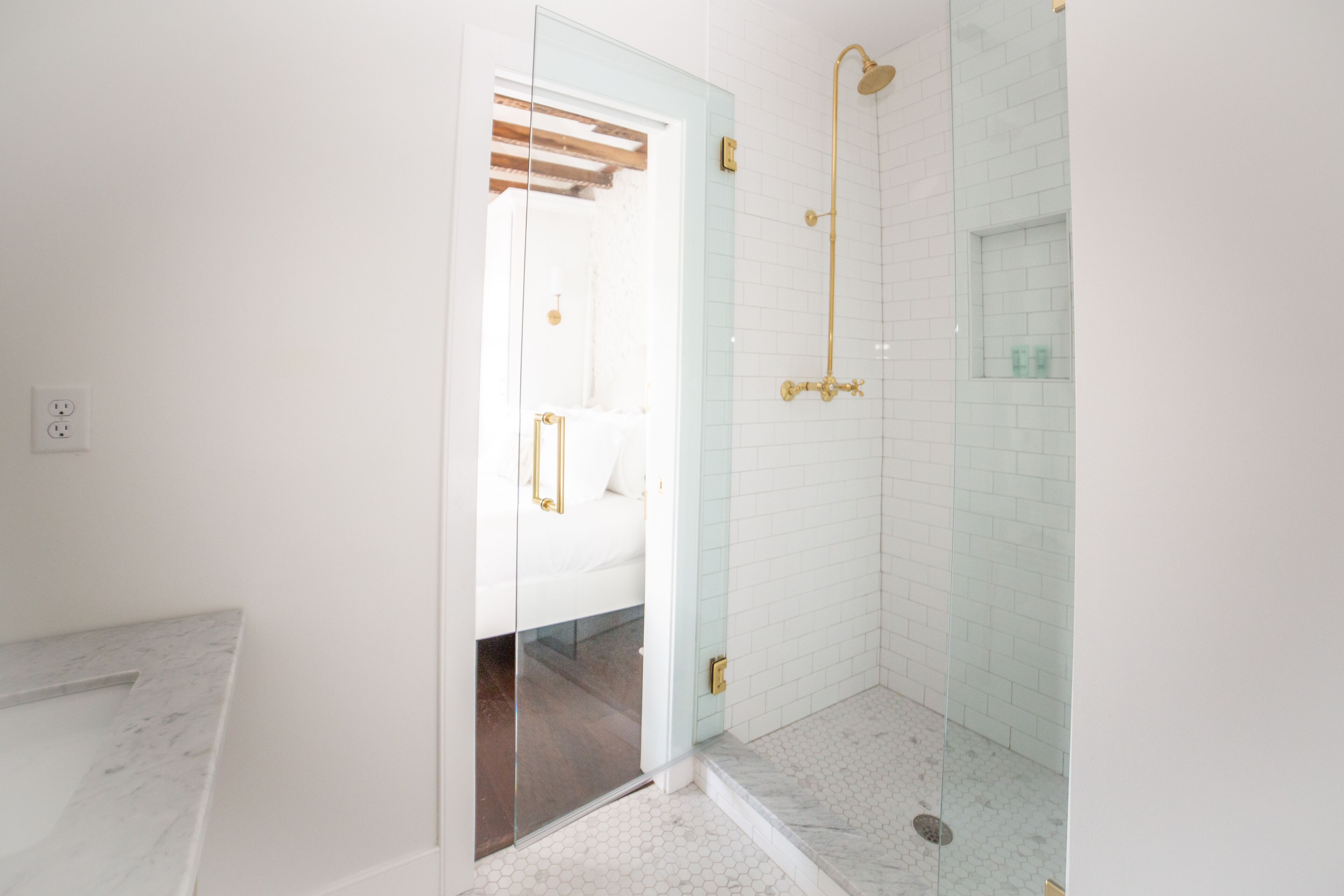 A modern bathroom with a glass shower enclosure, a marble countertop, and a white tiled wall.