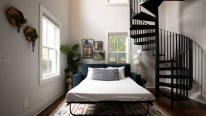 A bedroom with a bed, a black spiral staircase, a window, and a plant.