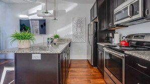 A modern kitchen with dark cabinetry, stainless steel appliances, and a granite countertop.