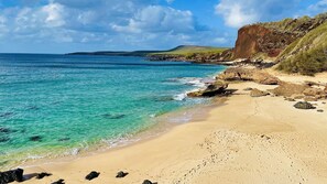 Una playa con aguas turquesas cristalinas, una orilla arenosa y acantilados rocosos.