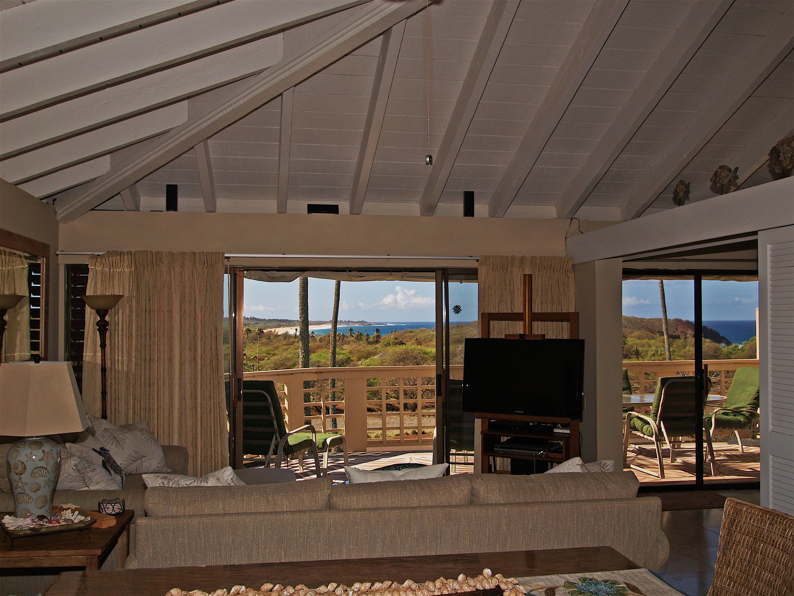 A spacious living room with a large sliding glass door leading to a balcony with a view of the ocean and hills.