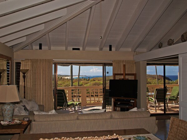 A spacious living room with a large sliding glass door leading to a balcony with a view of the ocean and hills.