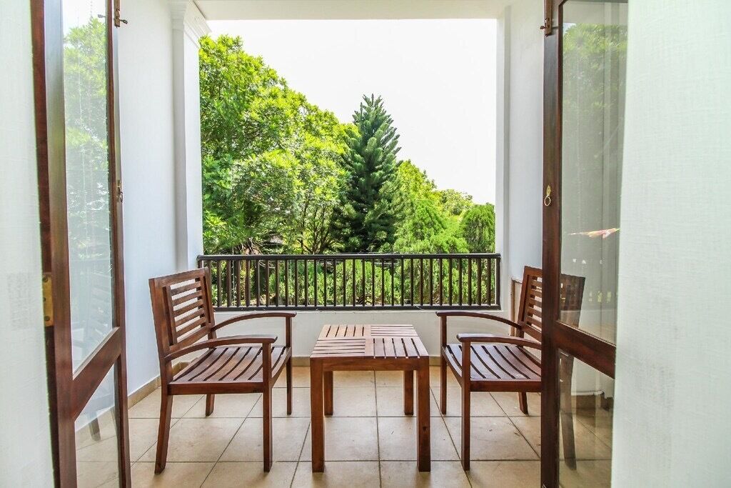 A balcony with a wooden table and chairs, overlooking a lush green area with trees.