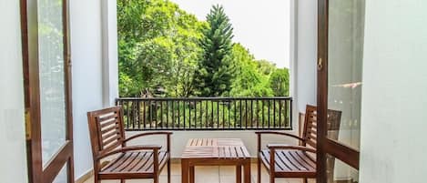 Un balcón con mesa y sillas de madera, con vista a una zona verde exuberante con árboles.