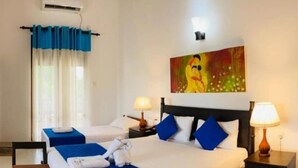 Ein Hotelzimmer mit zwei Betten, jeweils mit blauer Bettwäsche und weißen Kissen. Zwei Nachttische mit Lampen, ein Gemälde über den Betten und ein Fenster mit Vorhängen.