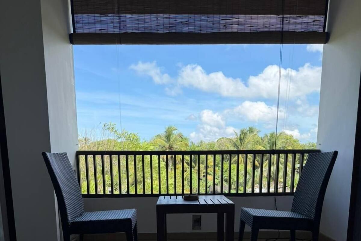 Een balkon met twee stoelen en een tafel, uitzicht op palmbomen en een betegelde vloer.