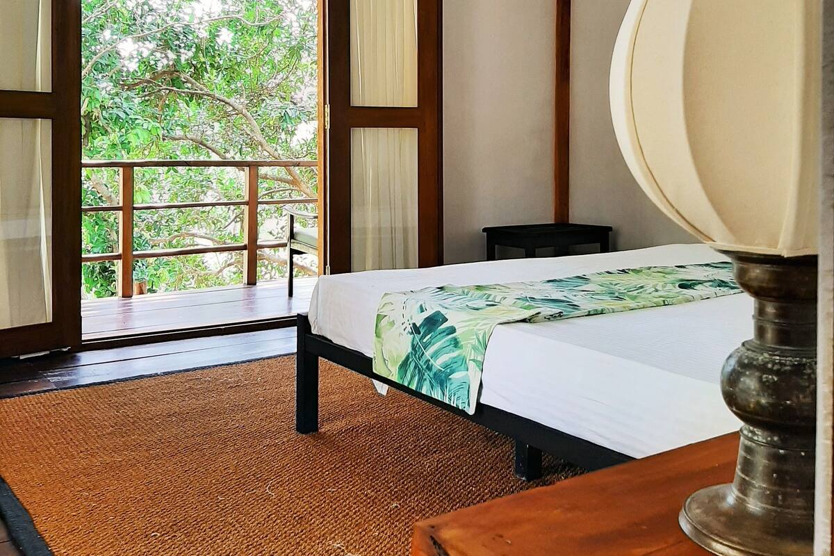A room with a bed, a wooden desk, and a window with curtains.