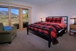 A bedroom with a large bed, a chair, a nightstand, and a view of a mountainous landscape through a sliding door.