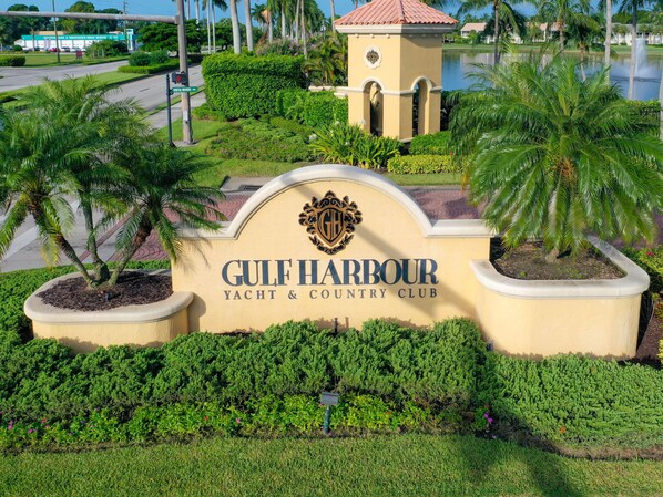 Placa para Gulf Harbour Yacht & Country Club, com entrada ajardinada com palmeiras e arbustos bem cuidados.