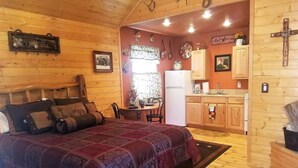 A wooden cabin interior with a bed, a dining table, and a kitchen area.