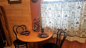A wooden dining table with two chairs, a vase with dried plants, and a coffee-themed curtain.