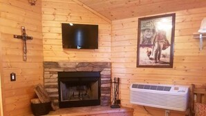 A log cabin interior with a stone fireplace, a mounted television, and a poster on the wall.