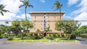 A multi-story hotel with a symmetrical facade, a central entrance, and a well-maintained garden with palm trees and shrubs. - Oceanfront Condo on magic Sugar Beach - Ocean View (Kihei)