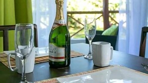 Een tafel gedekt voor twee personen, met een fles wijn, twee glaasjes en een witte mok.