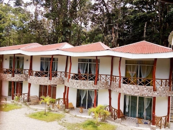 Fileira de edifícios de dois andares com varandas, cercada por árvores.