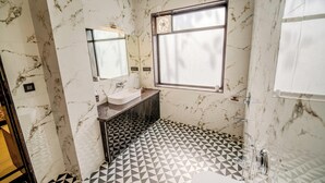 Ein Badezimmer mit Marmorwand, Waschbecken, Spiegel, Fenster und einem geometrischen Bodenbelag.
