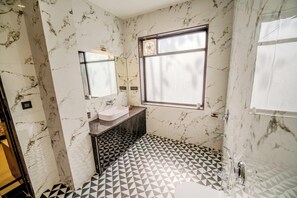 A bathroom with a marble wall, a sink, a mirror, a window, and a geometric patterned floor. - Kavish Holiday Hill Resort (Udaipur)