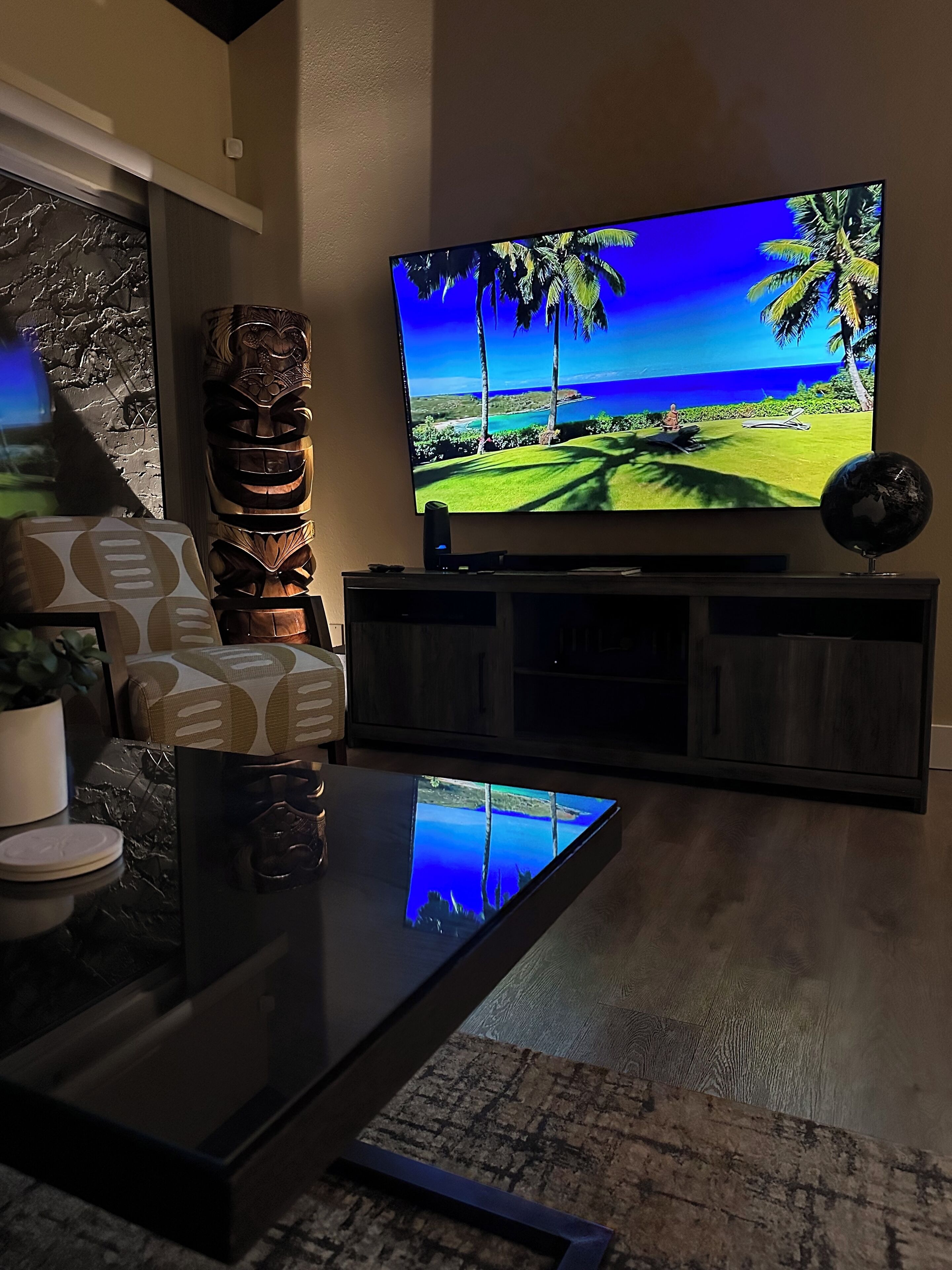 A living room with a flat-screen TV mounted on the wall, a dark wooden entertainment center, a patterned sofa, and a coffee table.