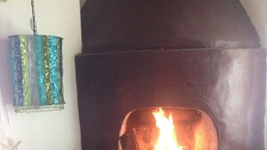 A fireplace with a fire, a mosaic-tiled wall, and a hanging decorative item.