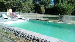 A rectangular swimming pool with a stone border, surrounded by a grassy area and trees.