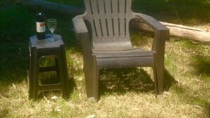 A chair and a stool in a grassy outdoor area with a bottle and glass on the stool.