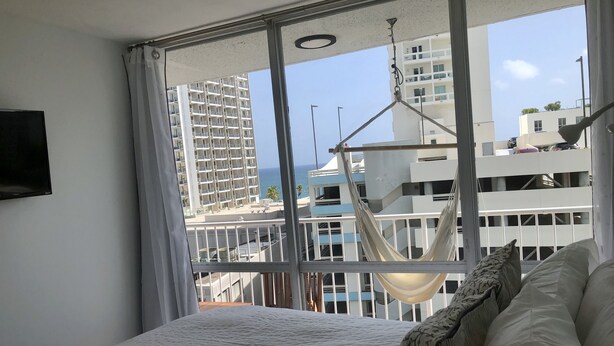 Een slaapkamer met een groot raam, een hangmat en een bed met kussens.