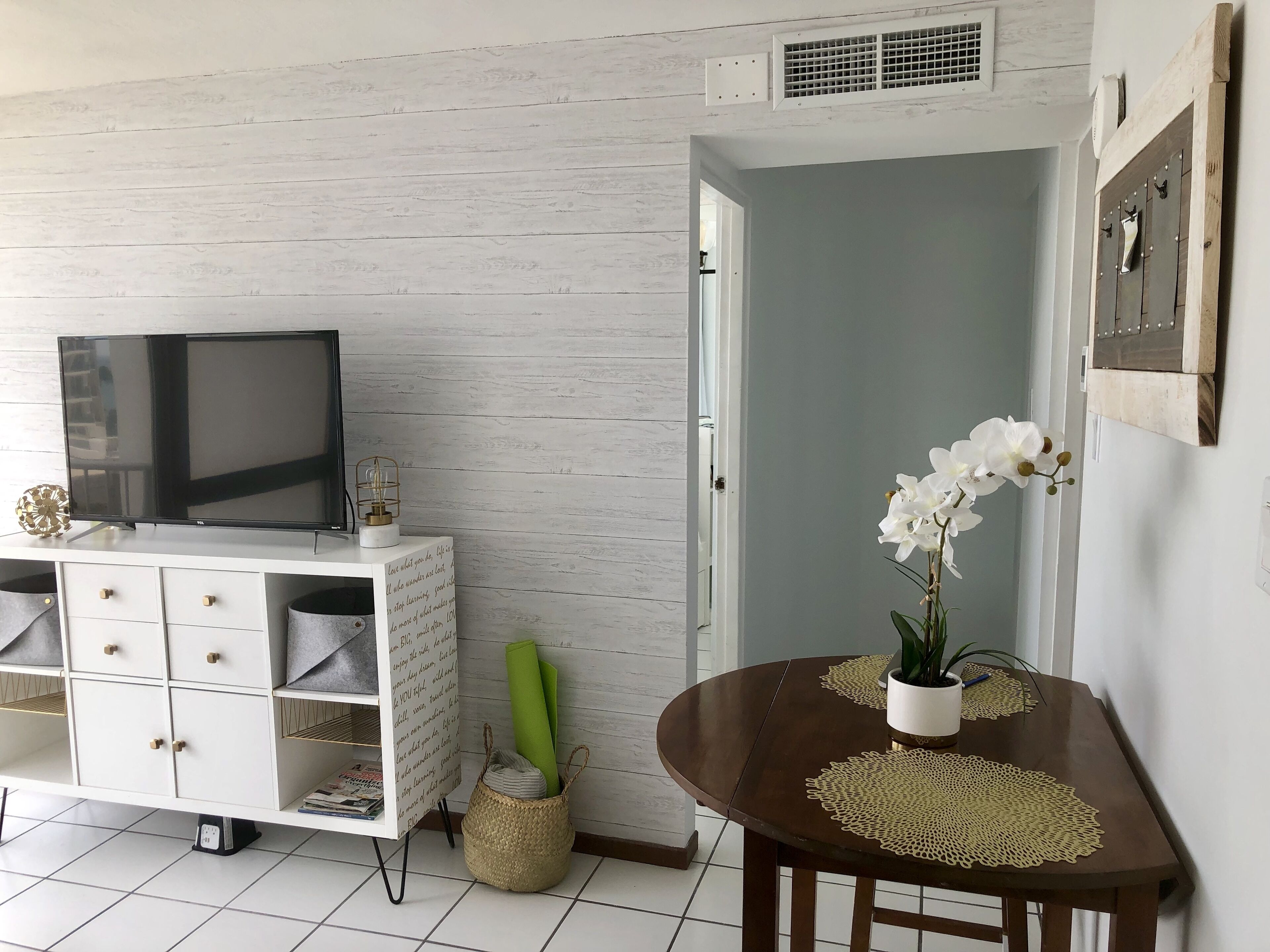 Une pièce avec un meuble blanc, une télévision, une porte et une table sur laquelle est posée une orchidée en pot.