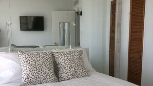 Een net opgemaakt bed met een gestreept kussen, een flatscreen televisie aan de muur en een spiegel die de kamer weerspiegelt.