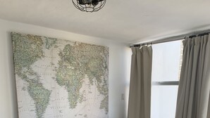 Een moderne woonkamer met een zwarte bank, een wereldkaart aan de muur en een raam met gordijnen.