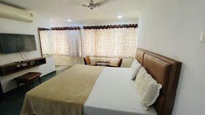 A hotel room with a bed, a TV mounted on the wall, a desk with a chair, and a window with curtains.
