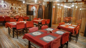 A restaurant with tables covered in red tablecloths, a mural of Buddha on the wall, and a patterned floor.