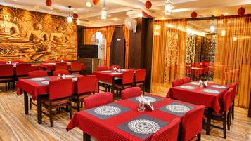 En restaurang med röda dukar och trästolar, en väggmålning med en Buddha och dekorativa hängande lyktor.