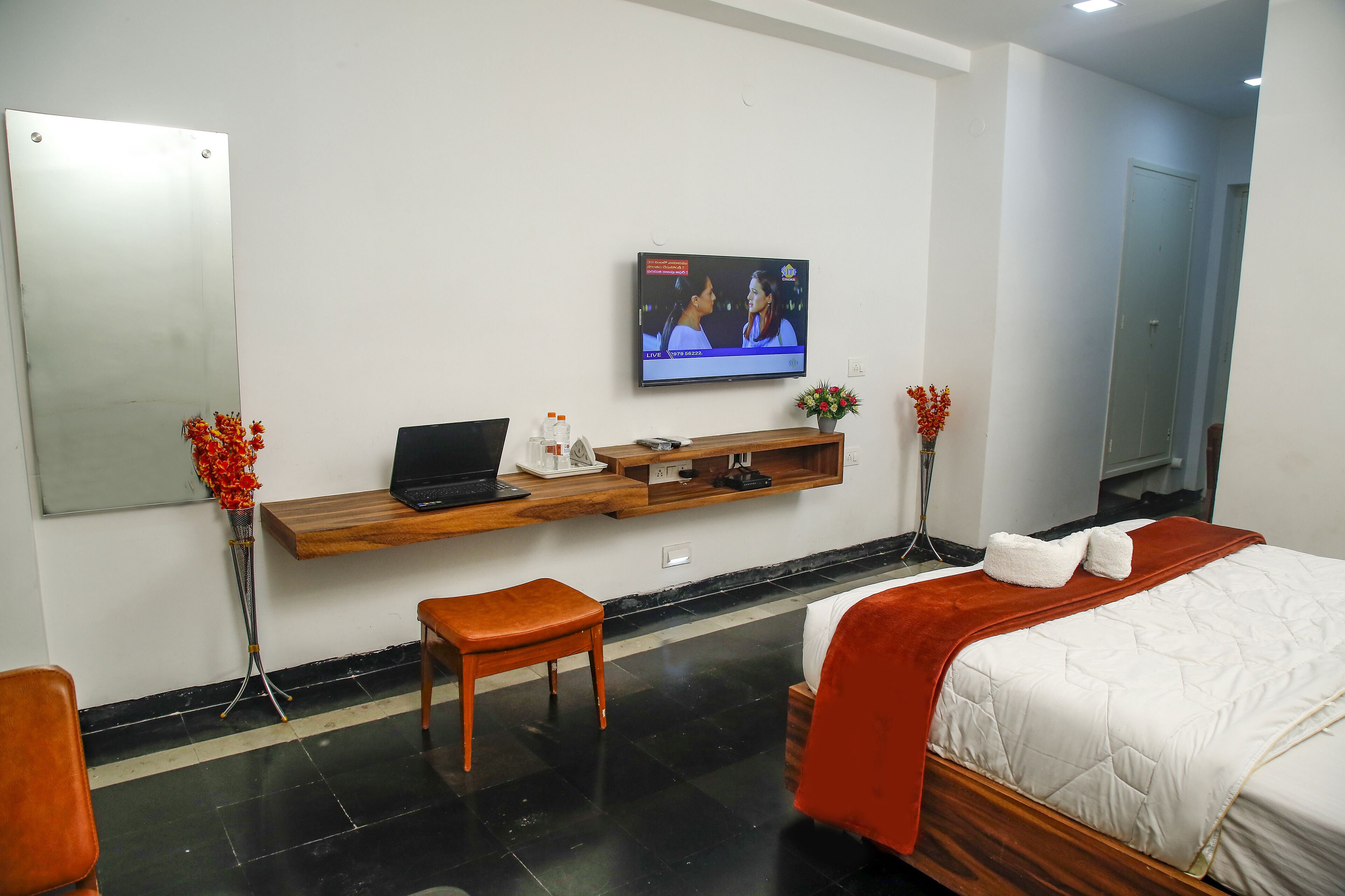 Une chambre d’hôtel avec un lit, un bureau avec un ordinateur portable, une télévision et deux vases de fleurs.