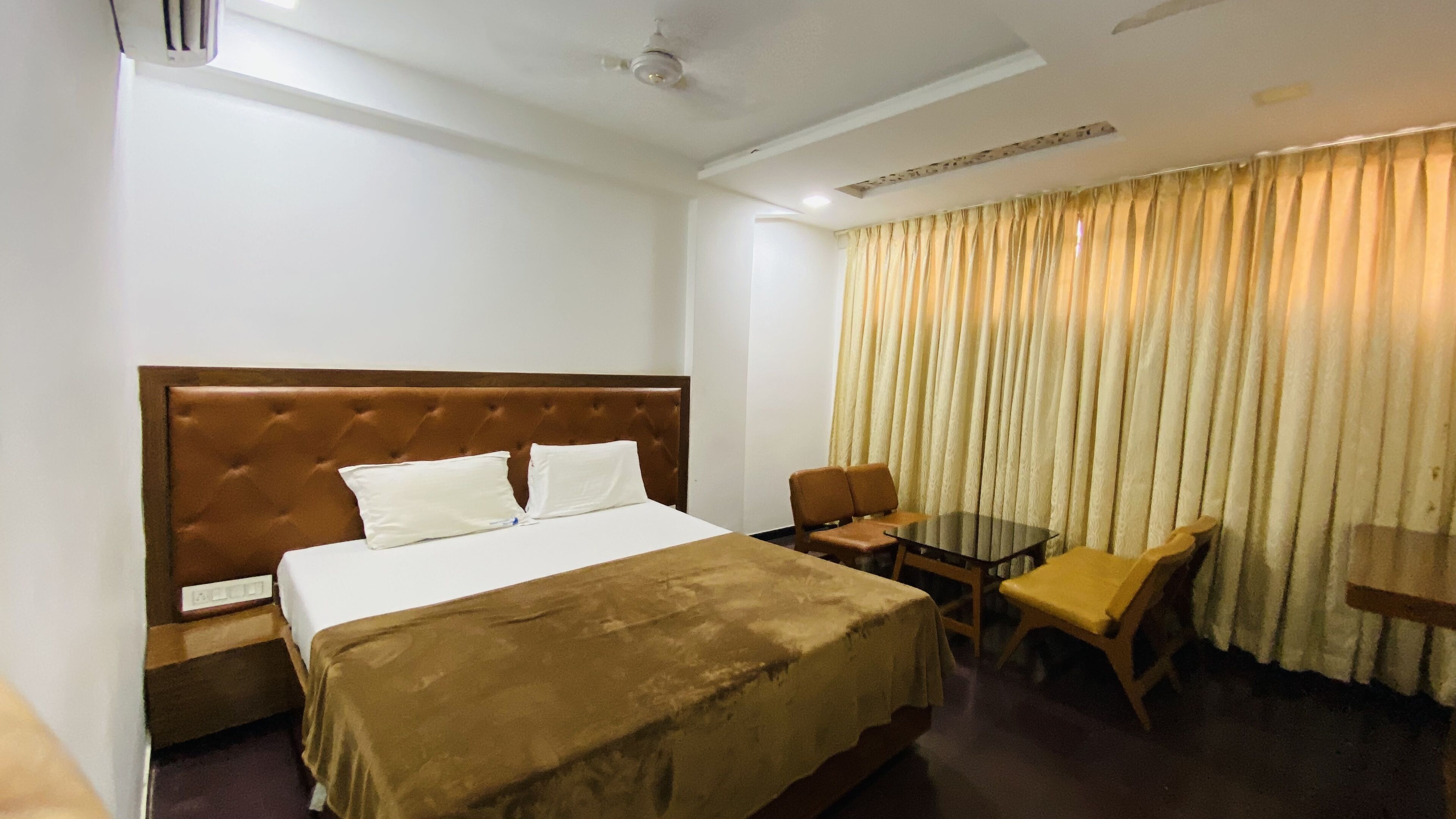 A hotel room with a large bed, a desk, two chairs, and a window with curtains.