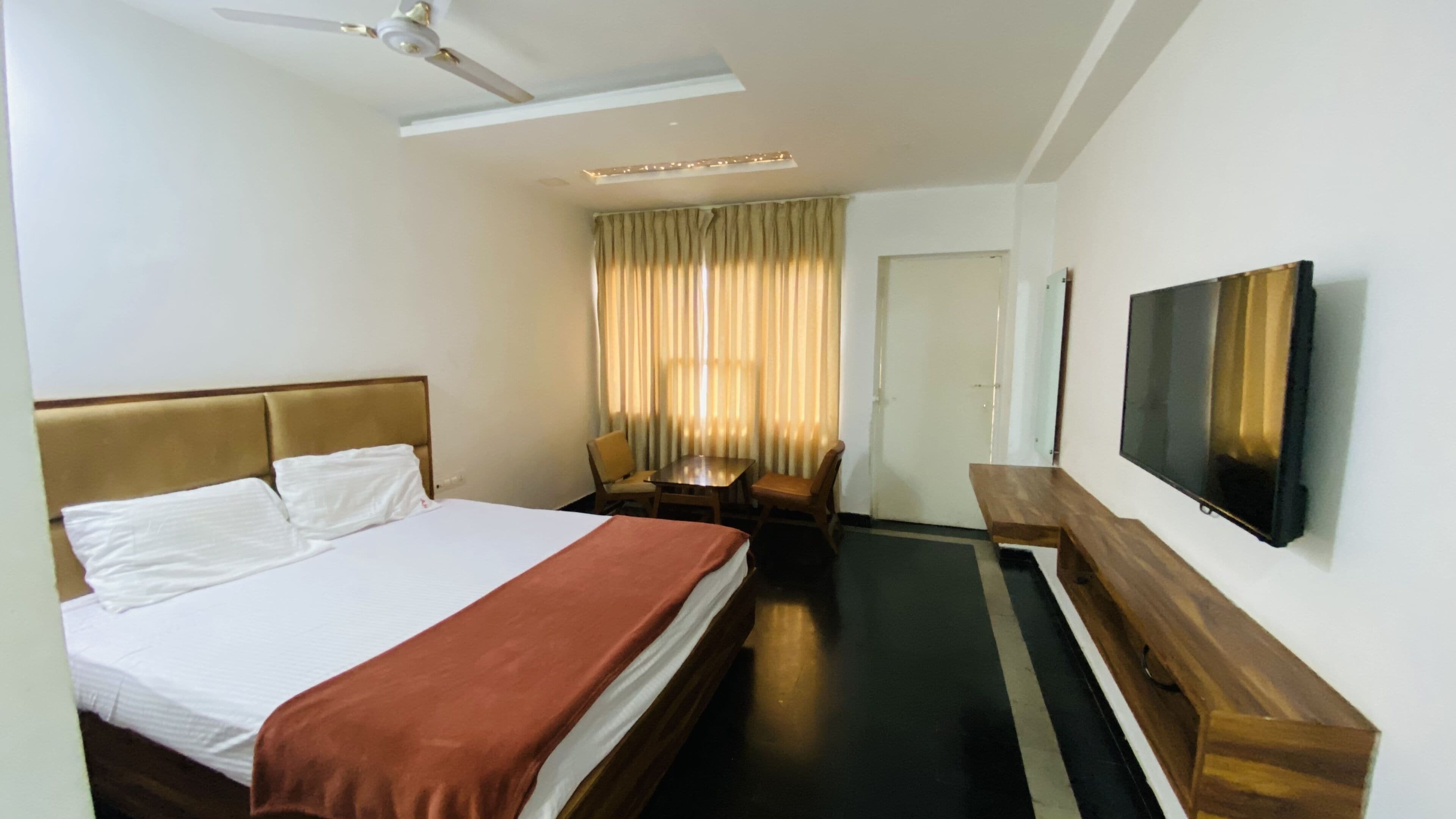 A hotel room with a bed, a desk, a chair, a television, and a ceiling fan.