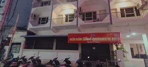 A hotel with a red signboard, balconies, and parked scooters. - Amaravathi Hotel (Guntur)