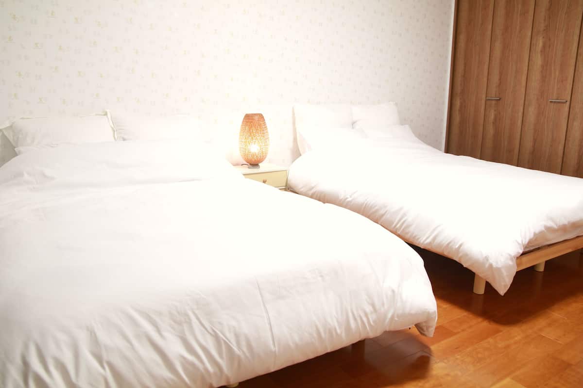 A bedroom with two beds, a nightstand with a lamp, and a wooden wardrobe.