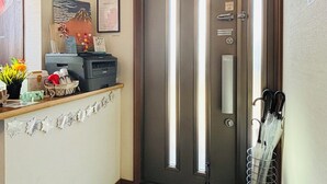 Un espace d’accueil d’hôtel avec une porte fermée, un petit bureau avec un ordinateur, un vase de fleurs et un panneau de signalisation indiquant la sortie de secours, fixé au mur.