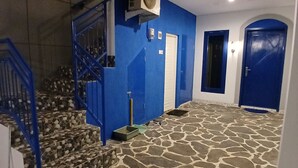 A staircase with blue railings leading to a stone-floored area with a blue door and an air conditioning unit mounted on the wall. - Moshi-Moshi - Hostel (Probolinggo)