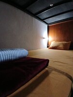 A single bed with a red blanket and a blue pillow in a room with a sloped ceiling and a wooden headboard.