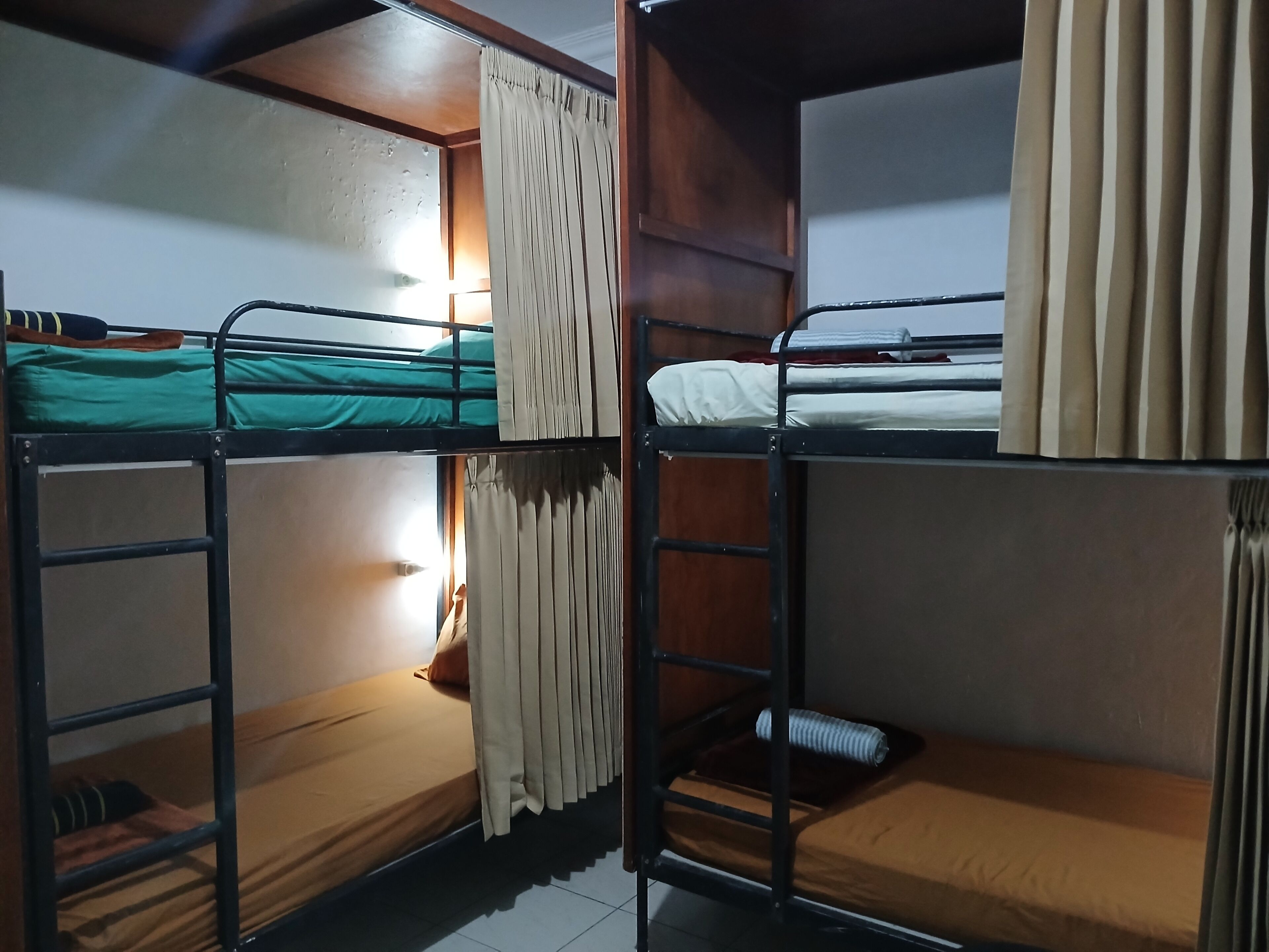 A dormitory room with bunk beds, wooden walls, and a curtain.