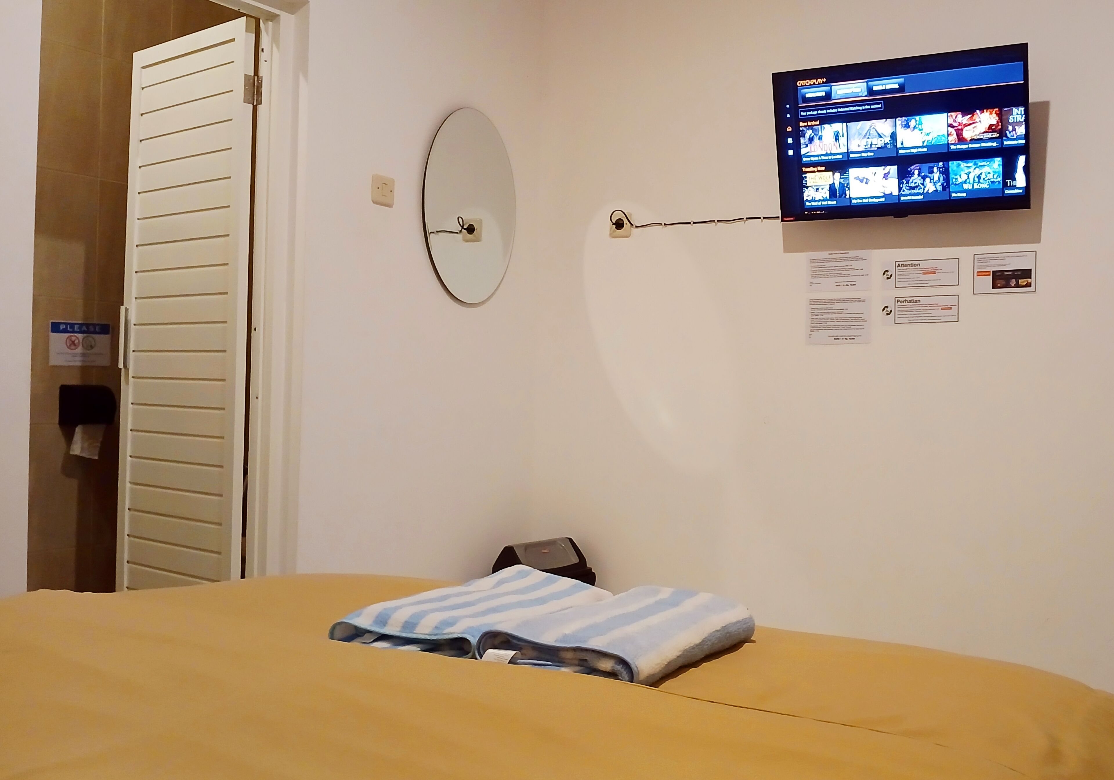 Habitació d'hotel amb llit, televisió penjada a la paret, mirall i porta.