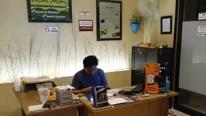 A reception desk with a man seated, a poster on the wall, and a sign indicating no outside food. - Moshi-Moshi - Hostel (Probolinggo)