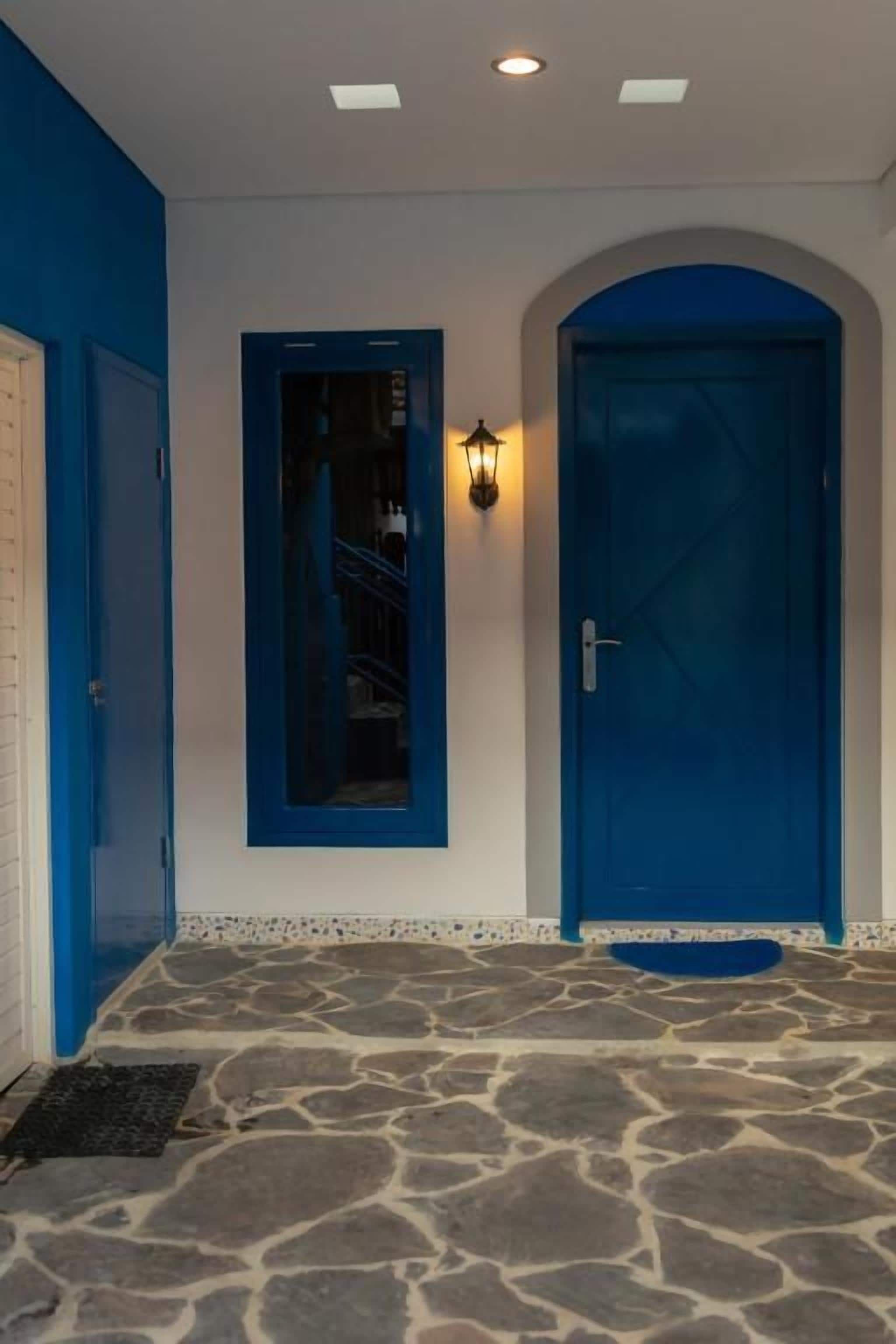 Un pasillo con una puerta azul, una lámpara de pared y un suelo con diseño de piedra.